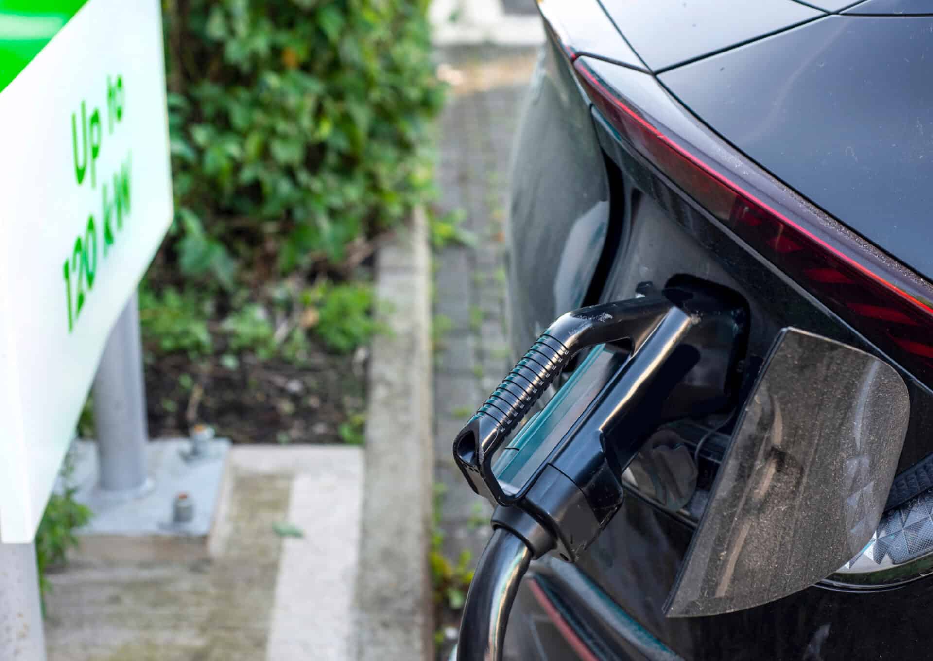 Parked domestic electric car,with charging connector attached ,being charged at a public electric vehicle charging location,situated within a public railway station car park.